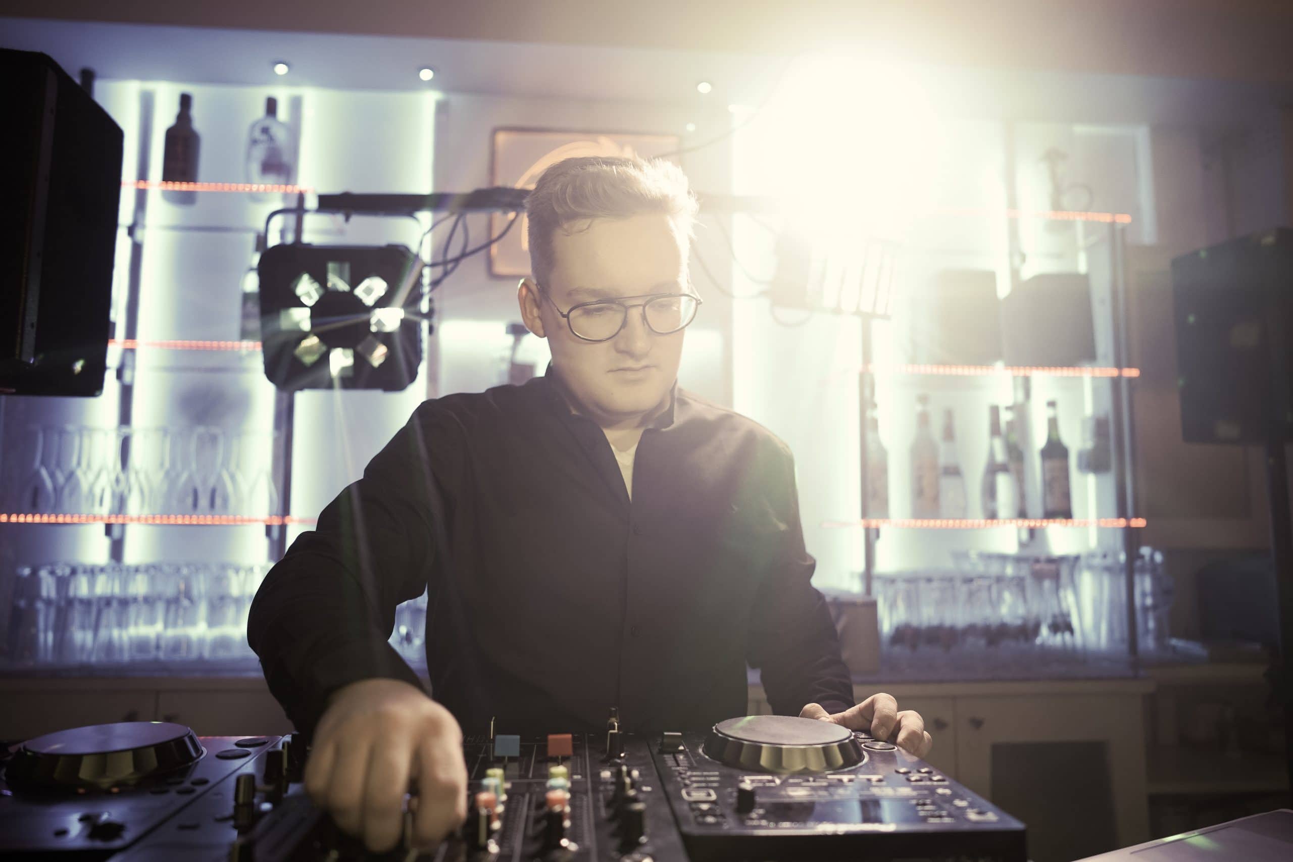 Elias Schreml DJ vor bunt beleuchtetem Hintergrund in einer Bar. DJ